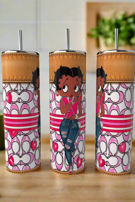 The Betty B Coach 20oz Skinny Tumblers by Kreative Kreationz feature a cartoon girl in pink and ripped jeans with heart, stripe, and loop designs. Eco-friendly stainless steel drinkware displayed on a wooden kitchen counter.