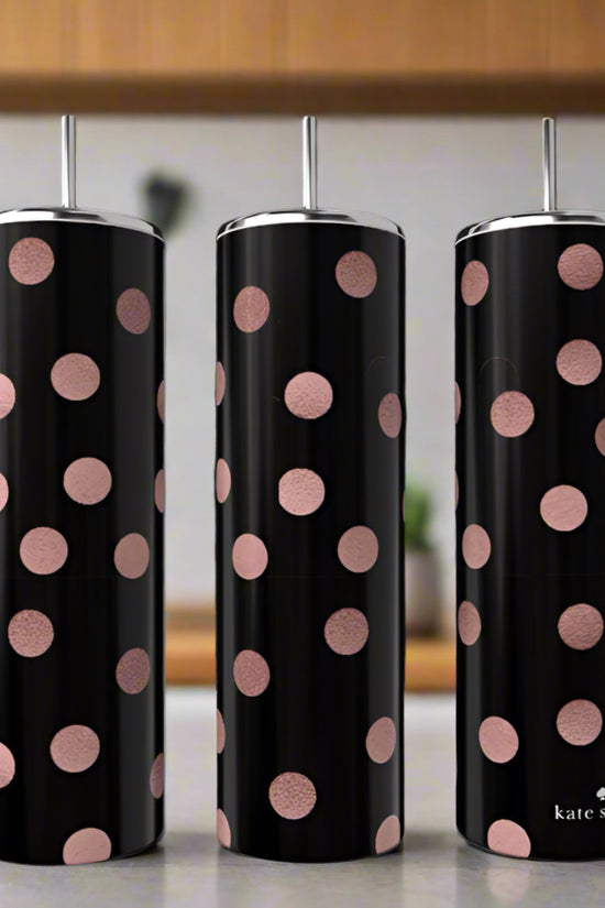 Three tall black luxury Kreative Kreationz 20oz tumblers with metallic lids and straws, decorated with large pink polka dots, sit on a kitchen counter amid blurred shelves and plants.