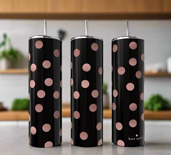 Three tall black luxury Kreative Kreationz 20oz tumblers with metallic lids and straws, decorated with large pink polka dots, sit on a kitchen counter amid blurred shelves and plants.