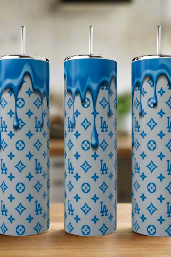 Three LV 20oz Tumblers by Kreative Kreationz, featuring blue dripping paint and luxury-inspired designs, stand side by side on a wooden surface, bringing an eco-friendly reusable style to the blurred kitchen backdrop.