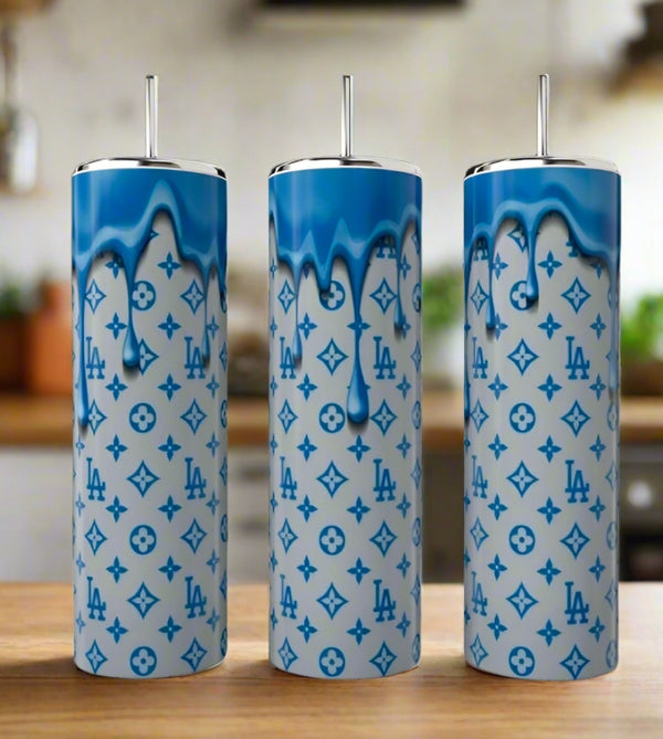 Three LV 20oz Tumblers by Kreative Kreationz, featuring blue dripping paint and luxury-inspired designs, stand side by side on a wooden surface, bringing an eco-friendly reusable style to the blurred kitchen backdrop.