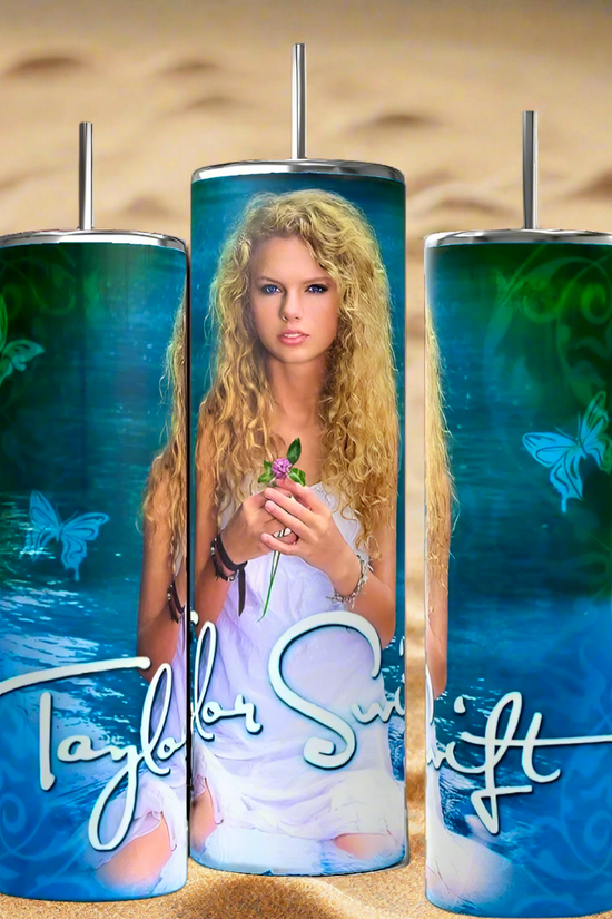 The Debut Taylor Swift 20oz Tumblers by Kreative Kreationz feature a person with long curly hair holding a pink rose against a blue-green butterfly background. The luxury-inspired design includes a stylized signature, set on sandy backdrop, and comes with reusable straws.