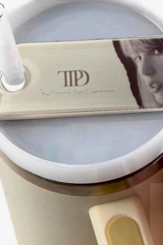 A round, white mug with a frothy drink features the TTPD Taylor Stanley Lid Topper from Kreative Kreationz, resembling a guitar pick with a face and 