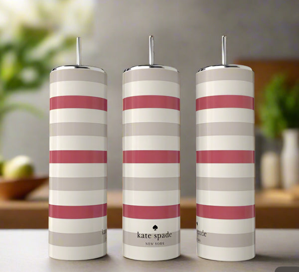 Three tall Kate Spade 20oz Skinny Tumblers by Kreative Kreationz, each with white, pink, and beige stripes and silver tops, are displayed on a table against a blurred background of plants and home decor.