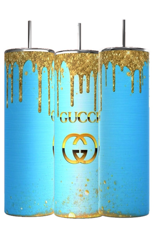The Kreative Kreationz Gucci Blue Drip 20oz Tumbler features a striking blue base with gold paint drips, resembling GUCCI's style. It bears a central gold logo and includes a spill-proof lid with an inserted metal straw for convenience.