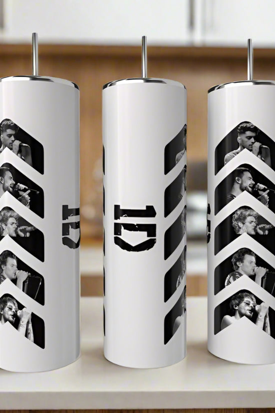 Three Kreative Kreationz 1D Play 20oz Tumblers with metal straws, each featuring black and white singing photos and a bold number 5 design, are lined up on a counter with a green plant in the background. Keeps drinks hot or cold.