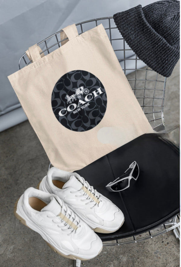 A wire chair displays a COACH Canvas Tote Bag by Kreative Kreationz, featuring a circular logo, surrounded by a gray knit beanie, white sneakers, and sporty sunglasses. The minimalist scene with its concrete floor and gray backdrop may captivate Swifties in search of style inspiration.