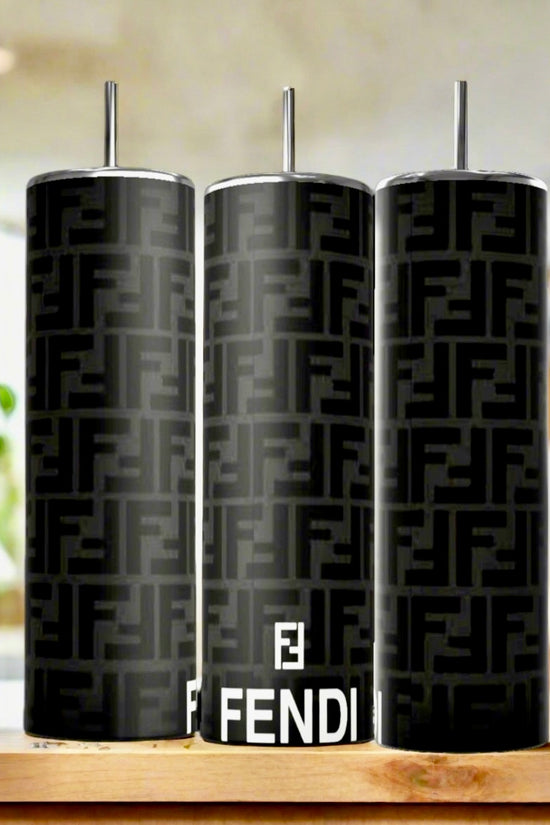 Three FENDI Black Grey Modern 20oz Skinny Tumblers by Kreative Kreationz, each with a metal straw, are lined up on a kitchen counter. The blurred background of plants and fruit accentuates these sleek, eco-friendly drinkware pieces.