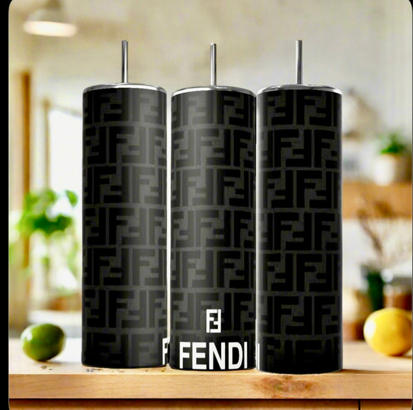Three FENDI Black Grey Modern 20oz Skinny Tumblers by Kreative Kreationz, each with a metal straw, are lined up on a kitchen counter. The blurred background of plants and fruit accentuates these sleek, eco-friendly drinkware pieces.