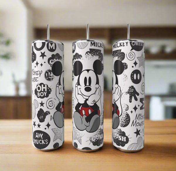 Three Kreative Kreationz Mickey Mouse 20oz Skinny Tumblers with black-and-white Mickey illustrations and phrases like “Oh boy!” and “Aw, shucks” are shown on a wooden surface with a blurred kitchen background.