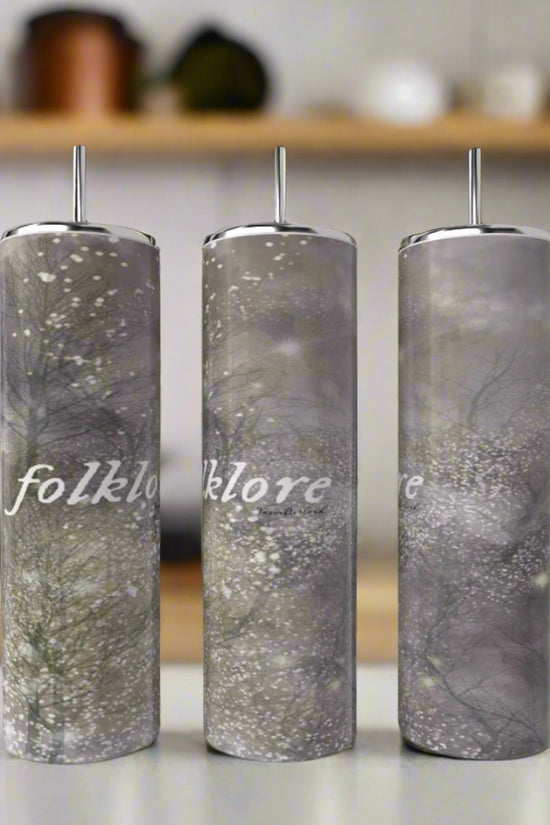 Three Kreative Kreationz Taylor Swift Folklore 20oz stainless steel tumblers with straws, gray forest design, and “folklore” in white script are displayed on a kitchen counter with blurred shelves in the background.