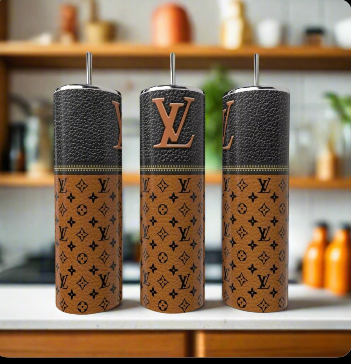 Three LV Brown Zipper 20oz Tumblers by Kreative Kreationz, featuring brown leather-like covers and black Louis Vuitton logos, stand on a kitchen counter, highlighting eco-friendly stainless steel style against a softly blurred background.