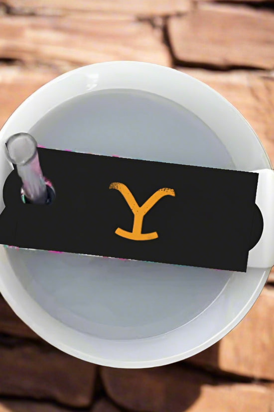 The white Yellowstone Stanley Lid Topper cup by Kreative Kreationz, partially encased in black paper with a yellow 