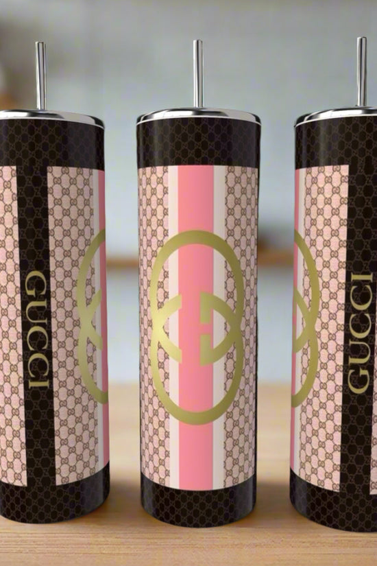 Three Gucci Pink 20oz Skinny Tumblers by Kreative Kreationz, featuring pink, beige, and black Gucci-inspired patterns and logos, are displayed on a wooden surface with blurred kitchen items in the background.