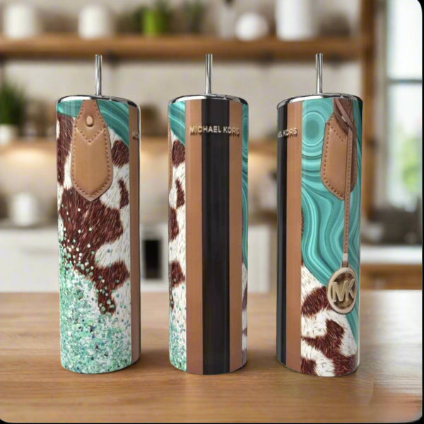 Three MK Hide 20oz Tumblers by Kreative Kreationz, each with a metal straw, rest on a wooden counter. The luxury drinkware showcases turquoise marbling, cowhide design, leather-like accents, and an MK logo medallion. A kitchen blurs behind.