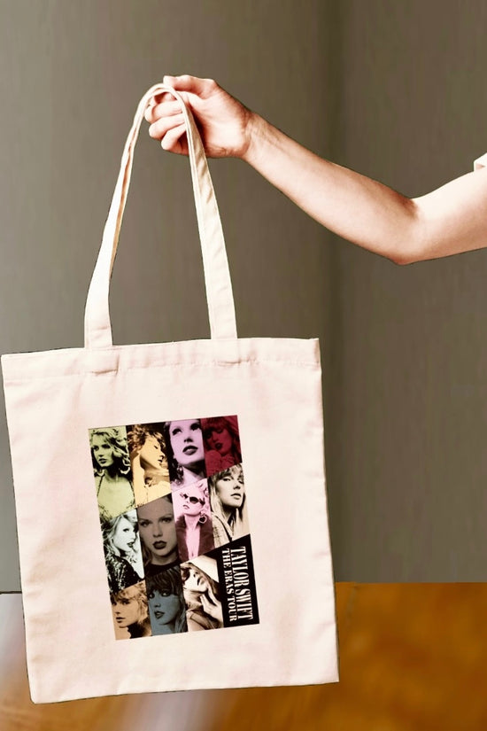 A hand holds the Kreative Kreationz Eras Tote Bag, featuring vibrant pop-art portraits of Taylor Swift and 