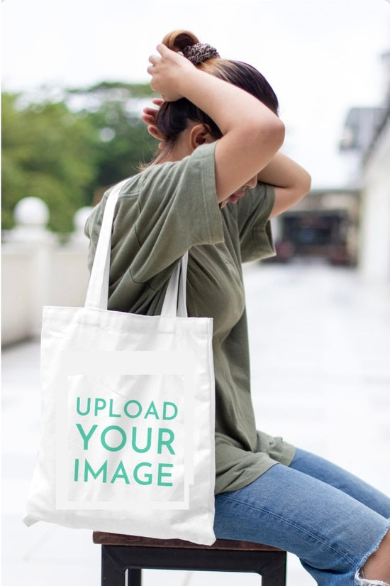 Outdoors, a person ties their hair back while wearing a green t-shirt, ripped jeans, and carrying the Tote-ally Yours Canvas Bag by Kreative Kreationz—an eco-friendly, roomy tote printed with 