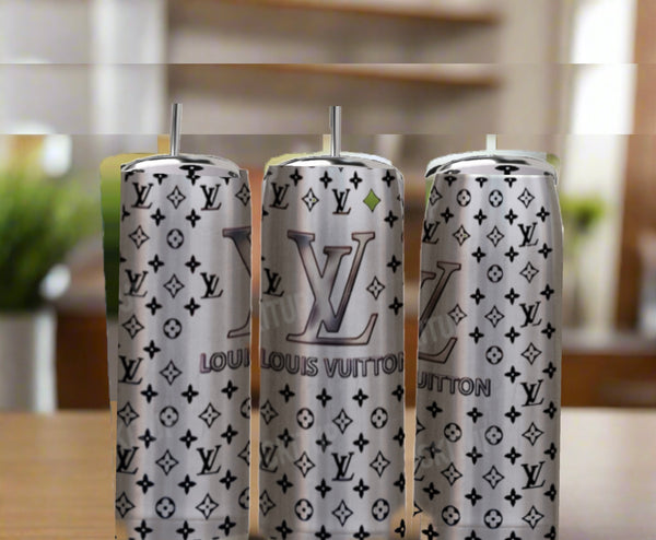 Three Kreative Kreationz LV Silver Stainless Steel Inspired 20oz Tumblers with silver straws sit on a wooden table. Each features a luxury gray Louis Vuitton-style monogram and logo against a softly blurred background.