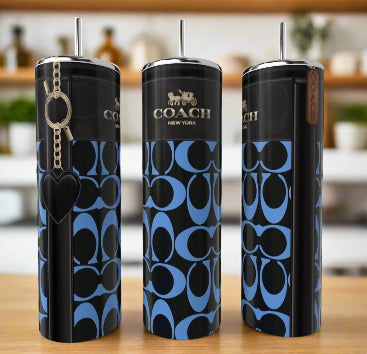 Three eco-friendly Coach Cobalt Blue Heart 20oz Skinny Tumblers by Kreative Kreationz, each with a stainless steel straw and blue-black Coach New York pattern, are displayed on a wooden surface; one includes a black heart keychain.