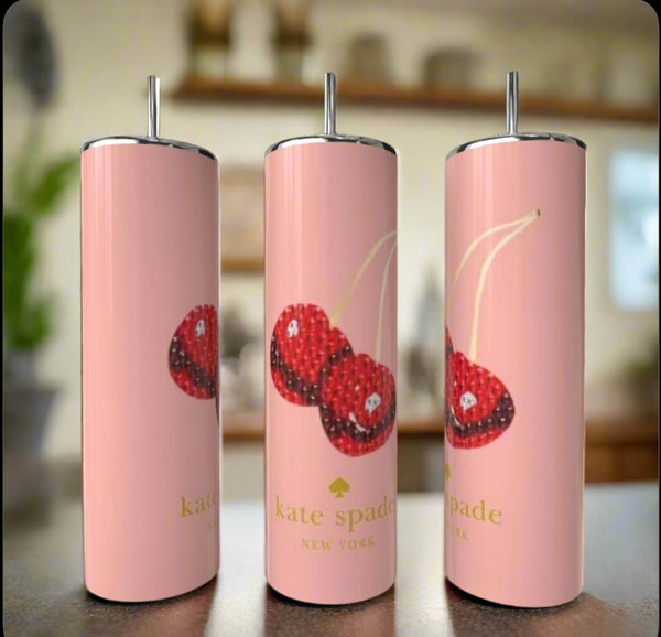 Three tall, pink Kreative Kreationz Kate Spade Cherry 20oz Skinny Tumblers with metal straws are displayed. Each features three cherry illustrations and a gold logo, set against a blurred background.