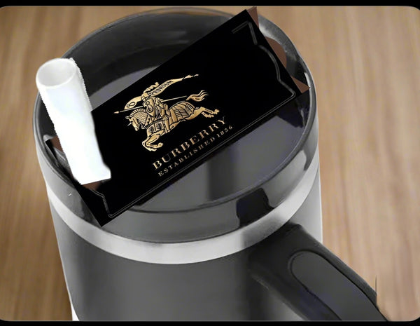 A Burberry | Stanley Lid Plate/Topper by Kreative Kreationz sits atop a black mug with a white straw, offering a chic designer touch—perfect for Stanley tumbler fans who love standout style.