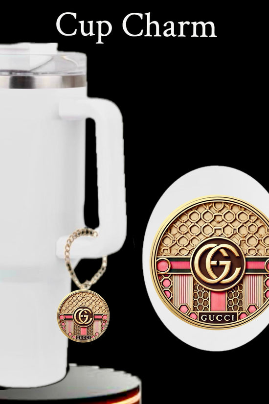 A white travel mug with a handle appears against a black background, adorned with the Kreative Kreationz Gucci | Pink Cup Charm featuring gold, pink, and red patterns and a central 