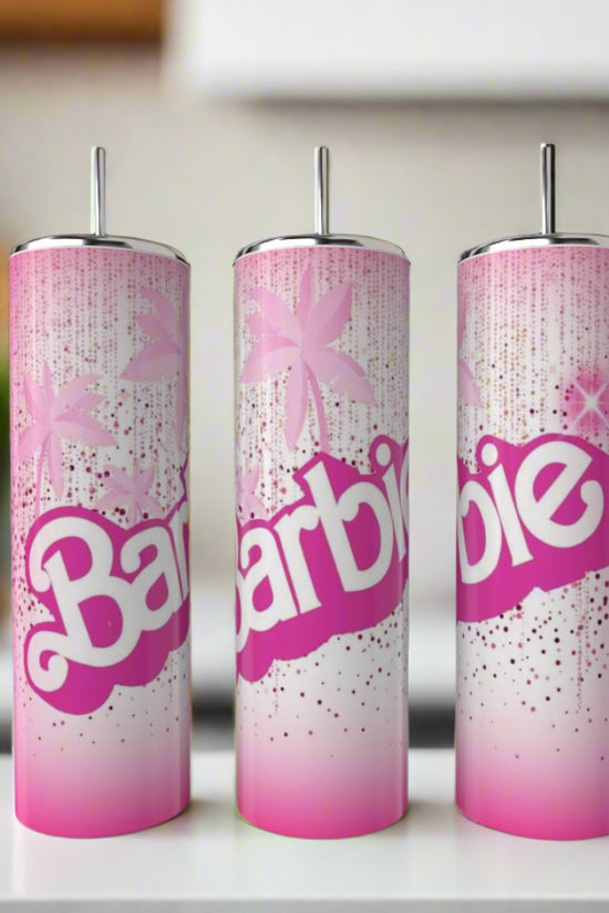 Three Kreative Kreationz Barbie 20oz Tumblers, featuring pink and white designs with bold “Barbie” lettering, sparkles, stars, silver lids, and straws, are shown on a white countertop in a modern kitchen.