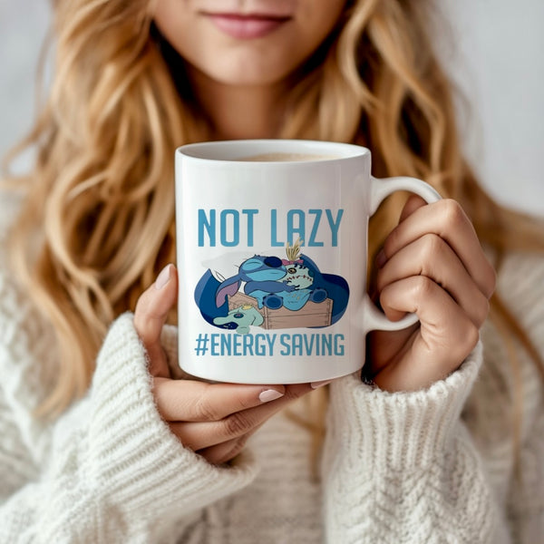 A woman in a white sweater holds the Stitch 15oz Mug by Kreative Kreationz, featuring a cartoon sloth lounging with the words “NOT LAZY #ENERGY SAVING” in a vibrant sublimation design close to her face.