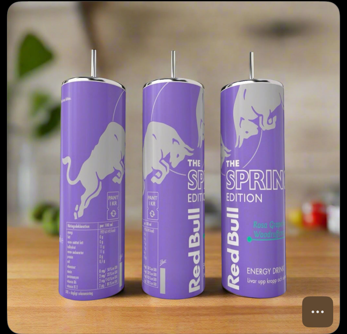 Three tall, lavender Kreative Kreationz Spring Red Bull 20oz Tumblers with silver bull graphics and eco-friendly reusable metal straws stand on a wooden surface, set against a blurred green background.