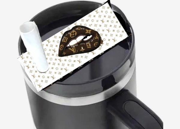 The Louis Vuitton Drip Lips Stanley Lid Plate/Topper by Kreative Kreationz decorates a black mug with a handle, featuring stylized lips and LV-inspired patterns. A white straw extends from the lid.