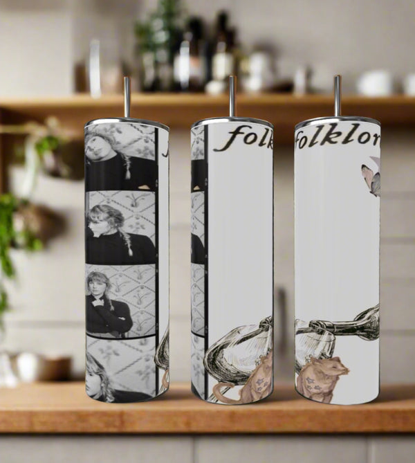 Three Kreative Kreationz Folklore Polaroid Taylor Swift 20oz Skinny Tumblers with straws sit on the counter, each featuring black-and-white Folklore photos, "folklore" text, and illustrated cats with an ink bottle.