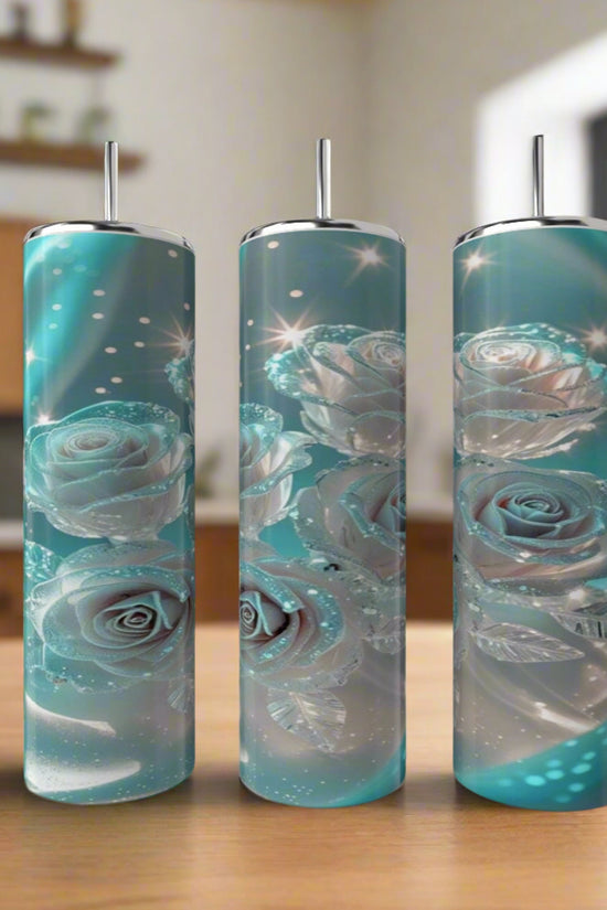 Three Kreative Kreationz Glowing Roses 20oz Stainless Steel Tumblers with straws, featuring glowing blue and silver roses and leaves, stand on a wooden surface in a softly blurred kitchen setting.