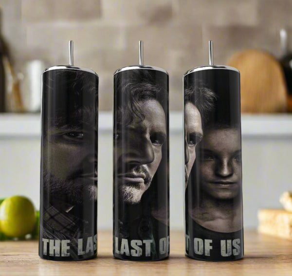 Three Kreative Kreationz CLast Of Us Fans 20oz Tumblers with straws feature close-ups of two "The Last of Us" characters and title text at the bottom. These eco-friendly tumblers are shown on a kitchen counter with blurred background items.