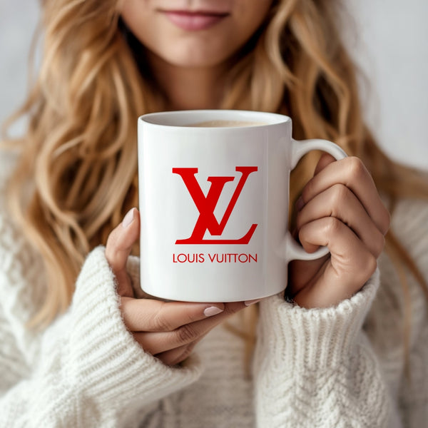 A woman in a cozy white sweater holds the LV Ceramic Mug by Kreative Kreationz, featuring a red Louis Vuitton-style logo, and smiles as she enjoys her drink.