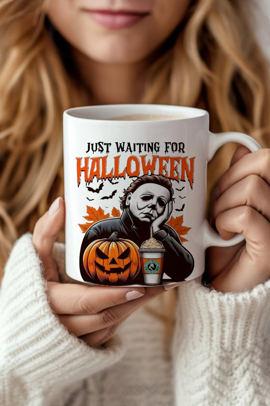 A woman in a cozy white sweater holds the Kreative Kreationz “Waiting For Halloween” ceramic mug, which features a spooky Michael Myers design with vibrant colors, bats, a jack-o’-lantern, and the phrase 