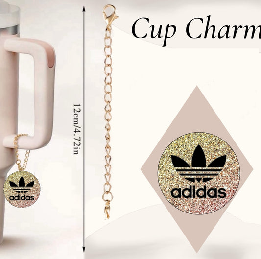 The Adidas Cup Charm by Kreative Kreationz is a handcrafted tumbler charm with a gold chain and round glittery charm featuring a black logo. It measures 12 cm (4.72 inches) and is displayed on a cup handle against a plain background with the text "Cup Charm.