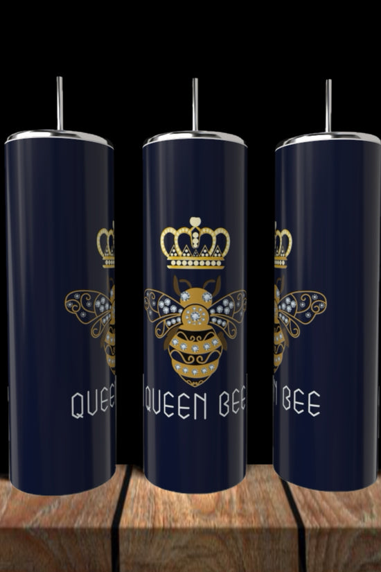 Three Kreative Kreationz Queen Bees 20oz Tumblers with silver lids and straws sit on a wooden surface, each featuring a gold crowned bee and the words “QUEEN BEE” in white on navy blue stainless steel.
