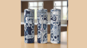 Three Kreative Kreationz Coach 20oz Skinny Tumblers with blue and white Coach patterns are displayed on a wooden surface. The eco-friendly, reusable stainless steel tumblers have straws inserted and a blurred indoor background.