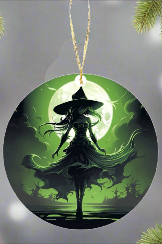 The Wicked Witch Christmas Tree Ornament from Kreative Kreationz dangles elegantly on the tree, featuring the silhouette of a witch with a flowing dress and hat set against a glowing green moon. This magical holiday decoration, nestled among evergreen branches, crafts a festive yet enchanting atmosphere.