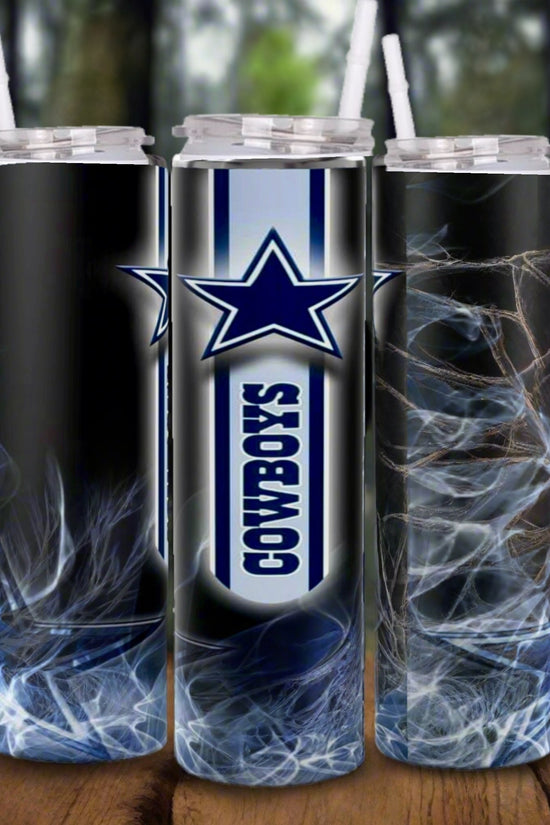 Three Kreative Kreationz Dallas Cowboys NFL Custom 20oz Skinny Tumblers with clear lids and straws, featuring the team's star logo and smoky abstract patterns, are displayed on a wooden surface with a blurred forest background.