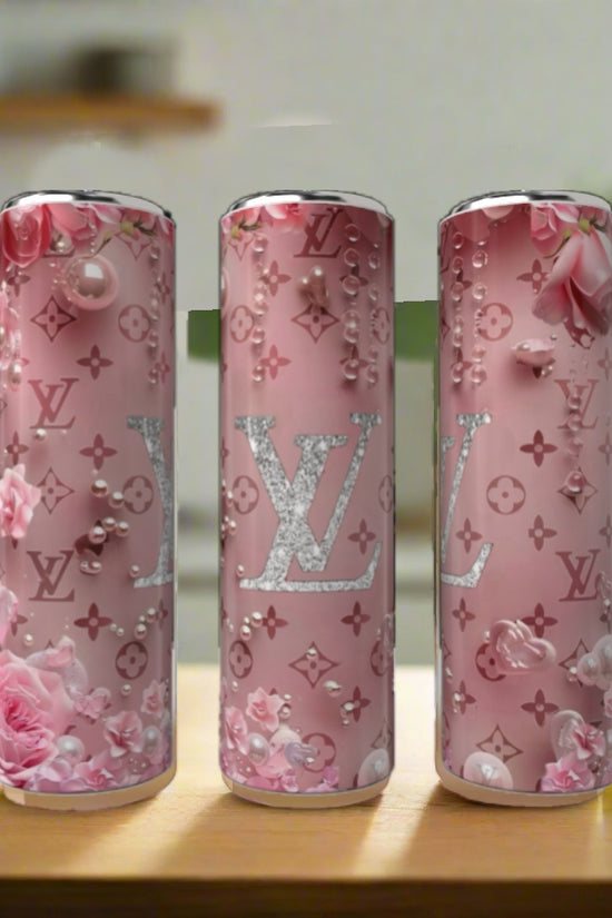 Three Kreative Kreationz LV Floral Pink 20oz Tumblers, decorated with floral and pearl designs plus bold “LV” logos, are displayed on a wooden surface in a bright kitchen.
