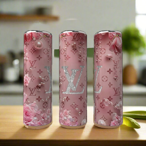 Three Kreative Kreationz LV Floral Pink 20oz Tumblers, decorated with floral and pearl designs plus bold “LV” logos, are displayed on a wooden surface in a bright kitchen.