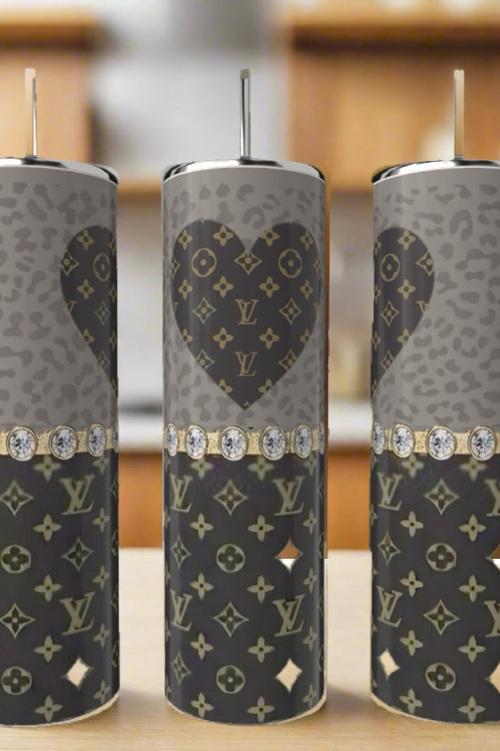 Three LV Heart 20oz Tumblers by Kreative Kreationz, featuring gray and black Louis Vuitton-inspired heart patterns and diamond-like bands, are displayed on a kitchen counter. These eco-friendly pieces add elegance to any setting.