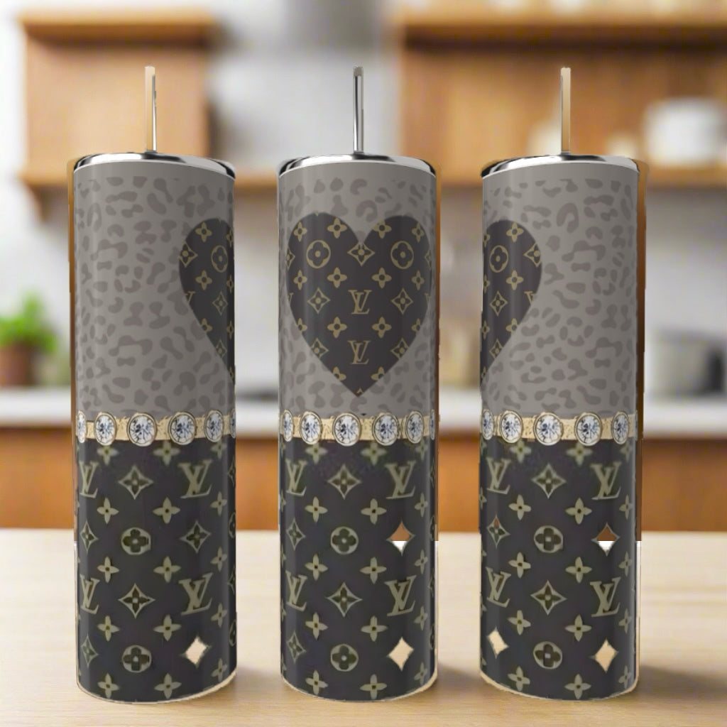 Three LV Heart 20oz Tumblers by Kreative Kreationz, featuring gray and black Louis Vuitton-inspired heart patterns and diamond-like bands, are displayed on a kitchen counter. These eco-friendly pieces add elegance to any setting.