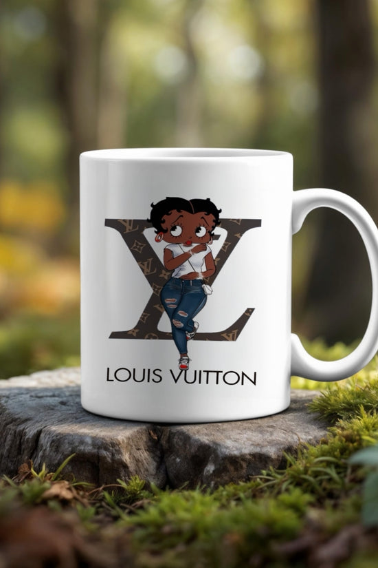 The Betty Boop LV Ceramic Mug by Kreative Kreationz features a cartoon girl before a large Louis Vuitton logo, set outdoors on a tree stump with a blurred forest backdrop—an ideal unique coffee or tea cup for your collection.