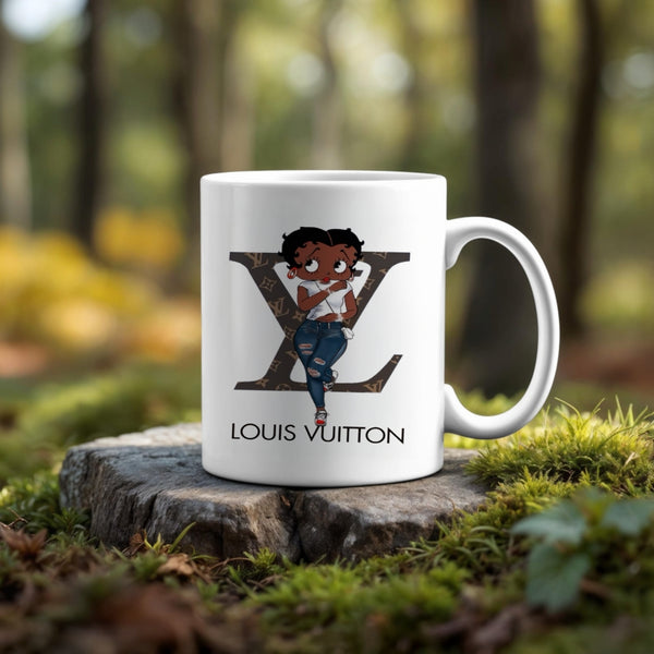 The Betty Boop LV Ceramic Mug by Kreative Kreationz features a cartoon girl before a large Louis Vuitton logo, set outdoors on a tree stump with a blurred forest backdrop—an ideal unique coffee or tea cup for your collection.