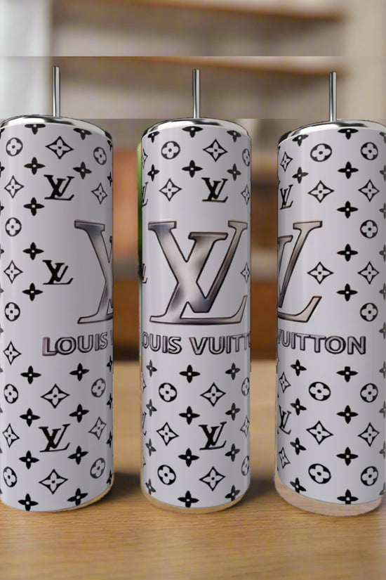Three LV Inspired Silver 20oz Tumblers by Kreative Kreationz, featuring stainless steel and a white and gray Louis Vuitton-inspired monogram, with straws, are displayed on a wooden surface against a blurred indoor background.