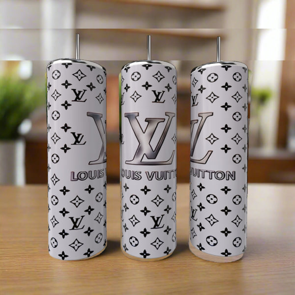 Three LV Inspired Silver 20oz Tumblers by Kreative Kreationz, featuring stainless steel and a white and gray Louis Vuitton-inspired monogram, with straws, are displayed on a wooden surface against a blurred indoor background.