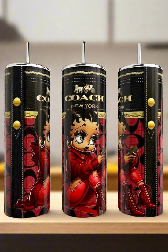 Three tall, black Kreative Kreationz Betty Boop 20oz tumblers with straws, each featuring a cartoon character in a red outfit with yellow buttons, are displayed on a counter against a blurred kitchen background.