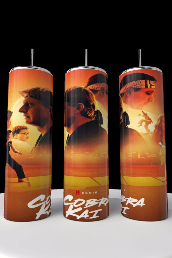 Three Kobra Kai 20oz stainless steel tumblers by Kreative Kreationz display vivid martial artists against a fiery orange backdrop, standing upright on a white platform that contrasts with the black background.